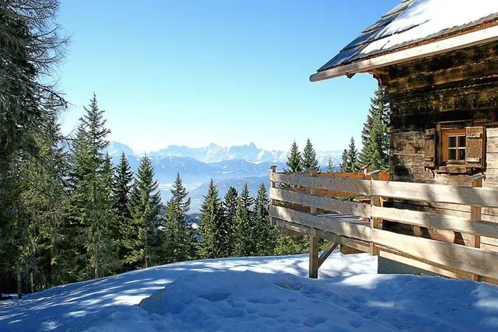 Snow-covered timber lodges of Lima Alpine Lodges in sunshine, with mountain ridges in the distance