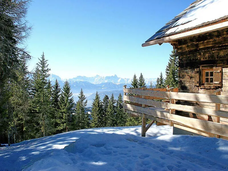 Snow-covered timber lodges of Lima Alpine Lodges in sunshine, with mountain ridges in the distance