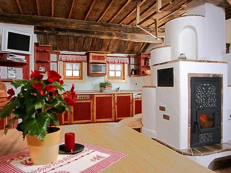 Kitchen and dining area in Troadkasten Lisa, with a white tiled stove and red flowers on the table
