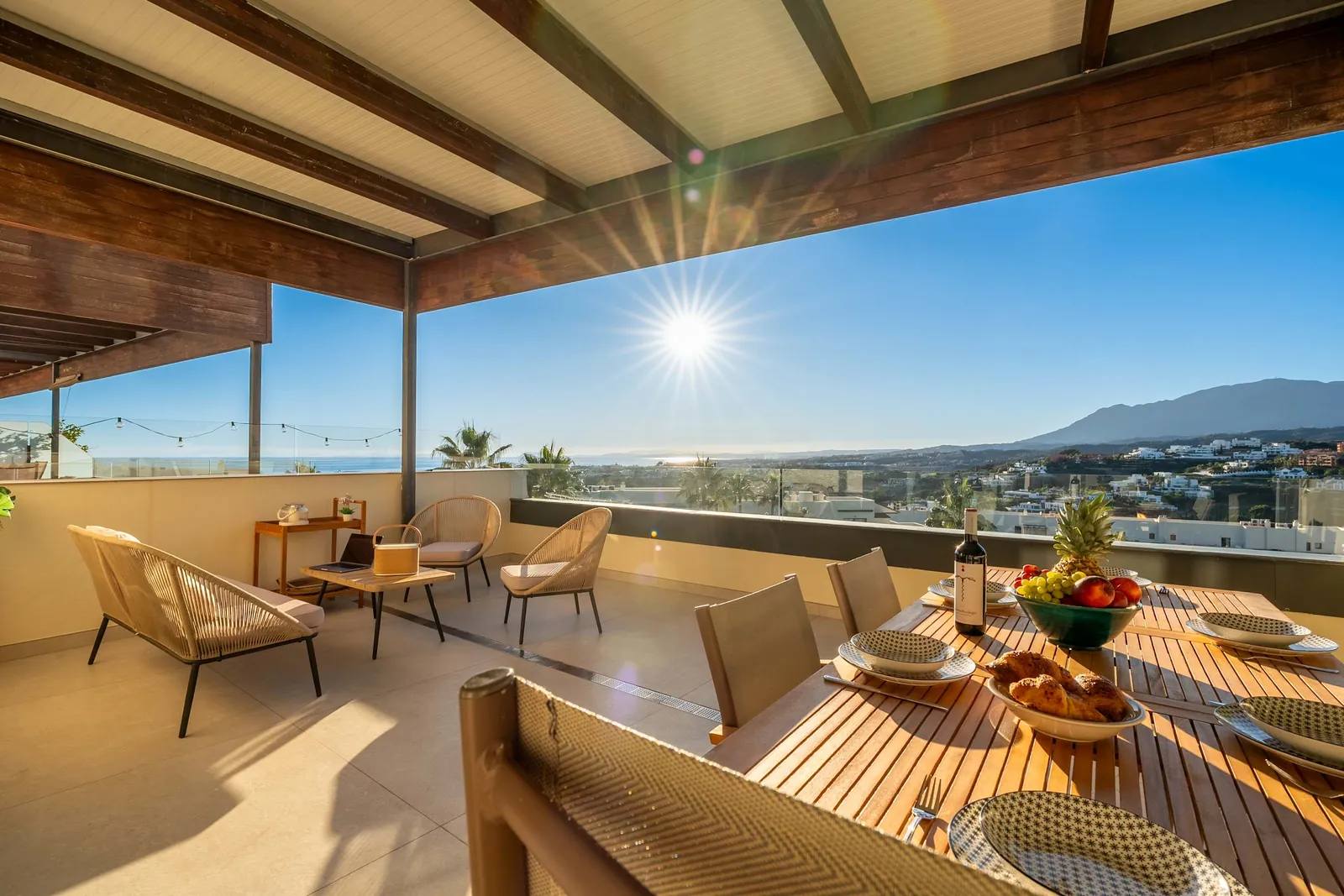 Covered terrace of the Luxury Escape apartment at Los Flamingos, with a laid dining table and a view across the coast towards the mountains