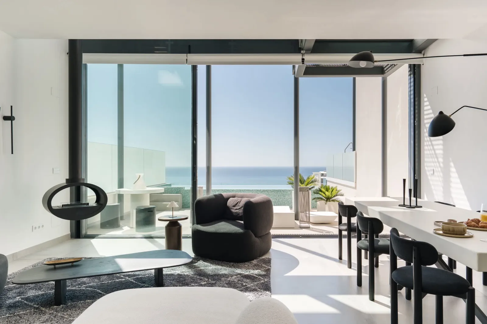 Living and dining area of the Higuerón infinity-pool villa, with a glass front opening onto a terrace above the sea