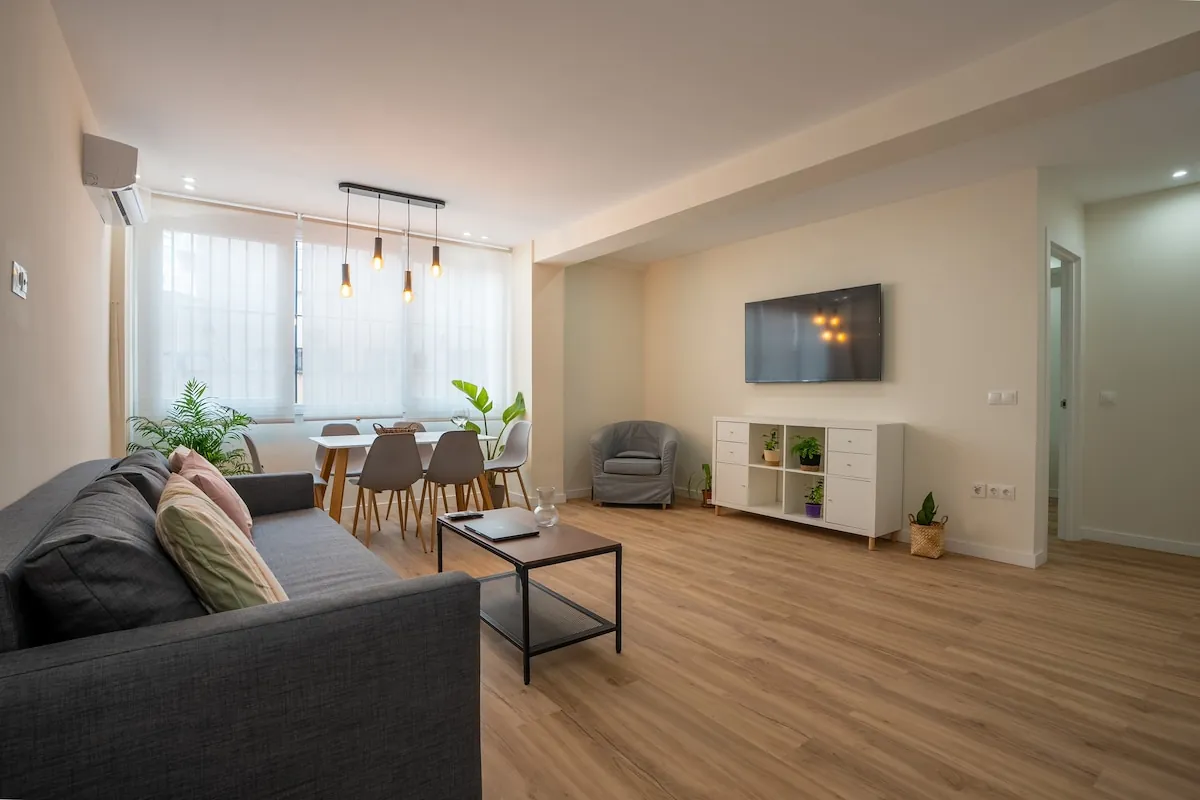 Living and dining area of the Soho Art Experience apartment, with a grey sofa, a dining table and parquet flooring